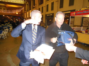 Brian Williams having just finished application of mustard to his hot dog is greeted by Steven  Levine from Wind Mill with an additional supply of hot dogs.